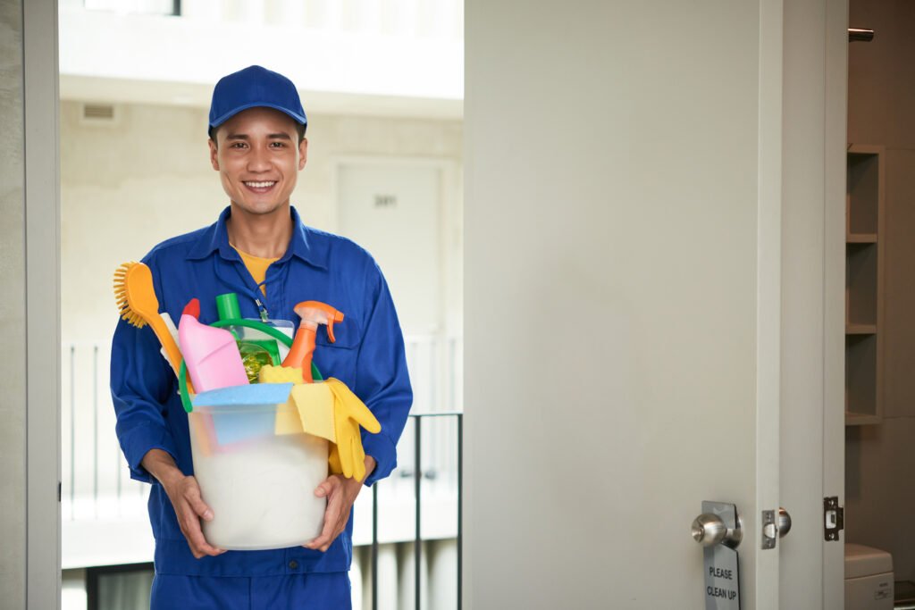 Cheerful Asian Male Janitor Walking Into Hotel Room Carrying Supplies Bucket 1024x683